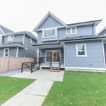 Modern Canadian suburban home with blue siding, manicured lawn, and backyard patio, showcasing Orca Realty Inc.'s expertise in Vancouver real estate.