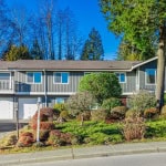 Spacious multi-storey home with attached two-car garage, surrounded by lush landscaping and mature trees, offering a charming residence in a peaceful neighbourhood.