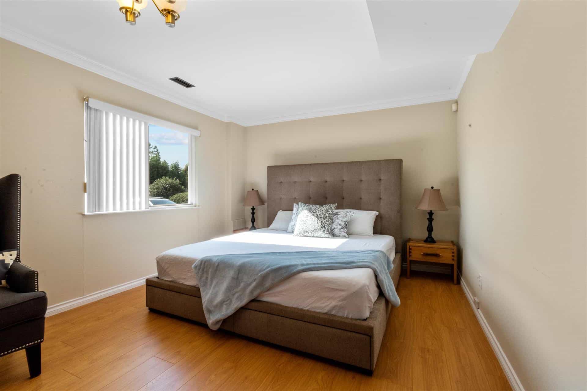 Bright, spacious bedroom with large window, beige walls, hardwood flooring, and modern furnishings, showcasing comfortable home interior in [Location] for real estate listings.