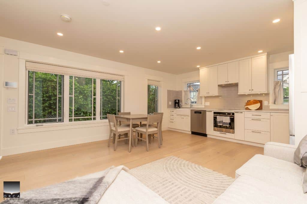 Bright, modern kitchen and dining area with large windows showcasing lush greenery, ideal for Vancouver Island real estate listings.