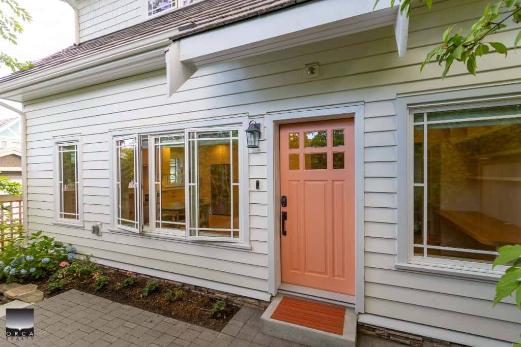 Charming white house exterior with pink front door, garden bed, and large windows, showcasing modern residential design and curb appeal in Ottawa.