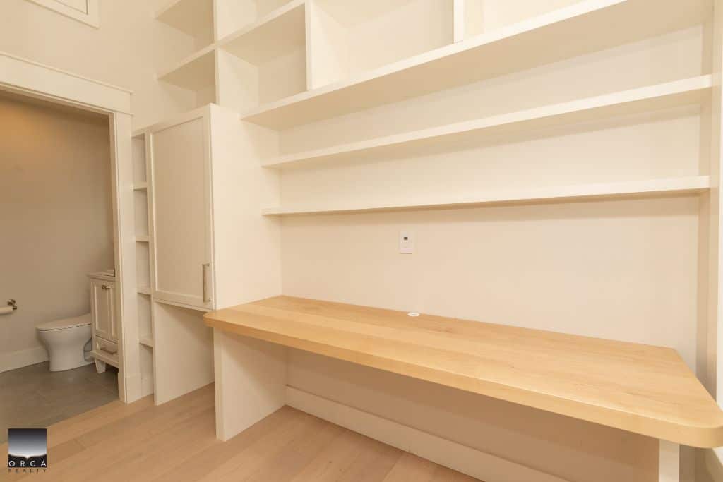 Spacious, modern home office with built-in shelving and natural wood countertop, ideal for remote work or study, located in a residential property listed by Orca Realty Inc.
