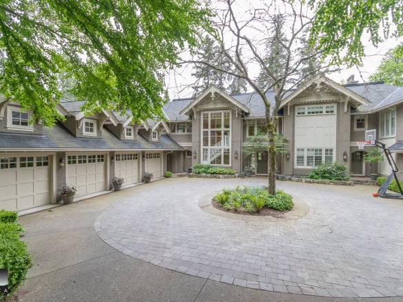 Spacious luxury home's front courtyard with a circular driveway, mature trees, lush landscaping, and a basketball hoop, showcasing elegant architecture and outdoor living space.