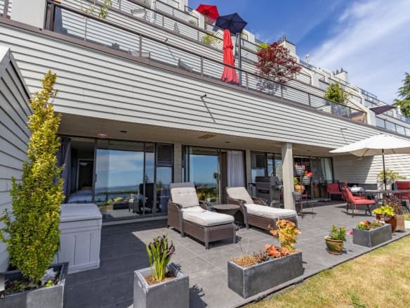 Modern outdoor patio with lounge chairs, potted plants, and a dining area overlooking scenic views, part of a contemporary residential building in Vancouver.
