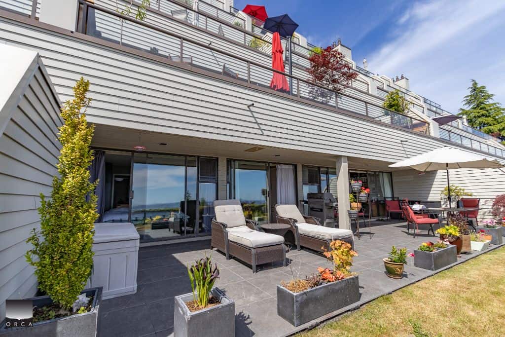 Modern outdoor patio with lounge chairs, potted plants, and a dining area overlooking scenic views, part of a contemporary residential building in Vancouver.