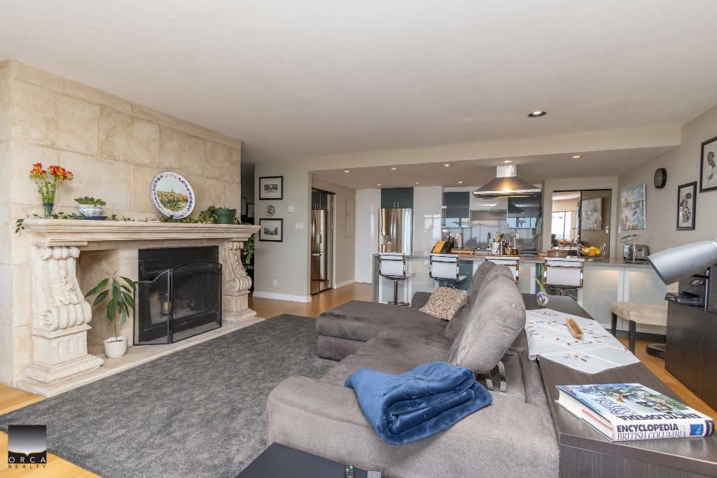 Modern living room interior with cozy grey sectional sofa, fireplace, and open-concept kitchen in a contemporary home, showcasing stylish decor and functional space, ideal for family living.