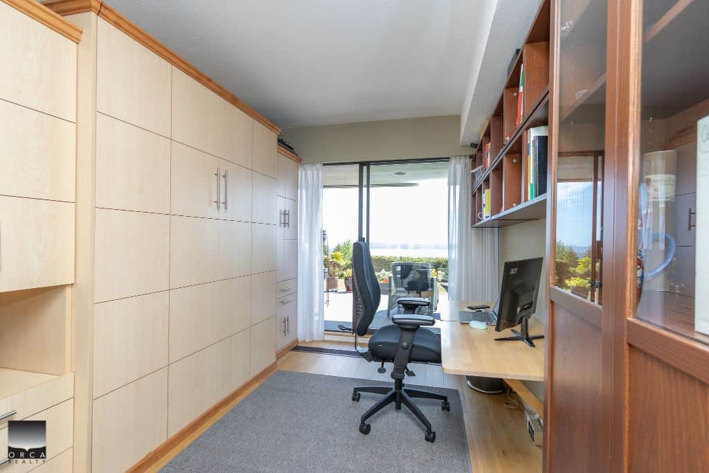 Bright home office with large window view, wooden and glass furniture, and ergonomic chair, ideal for productive real estate work and consultations.