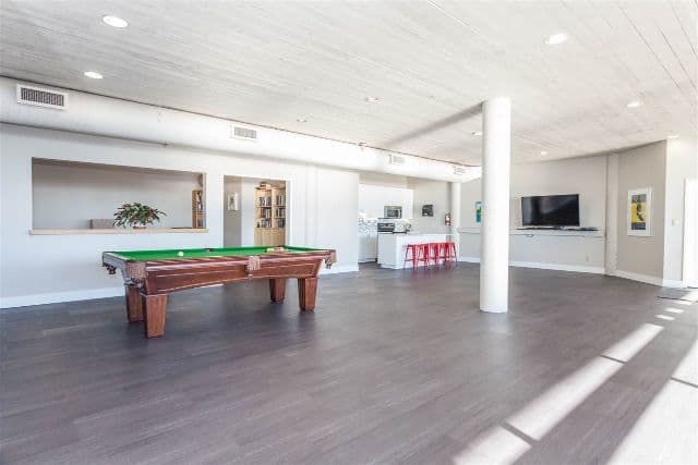 Modern residential lounge with pool table, contemporary decor, white walls, and large windows providing ample natural light, ideal for relaxation and social gatherings.