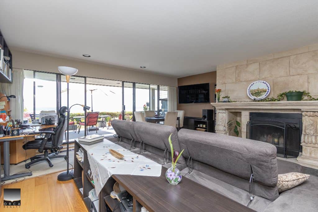 Bright living room with large windows, cozy fireplace, and contemporary decor, showcasing Vancouver Island home for sale with open-concept design and ocean views by Orca Realty Inc.
