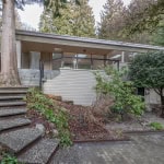 Spacious modern house with large glass windows, surrounded by lush trees and landscaped garden in a serene natural setting.