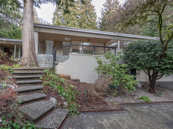 Spacious modern house with large glass windows, surrounded by lush trees and landscaped garden in a serene natural setting.