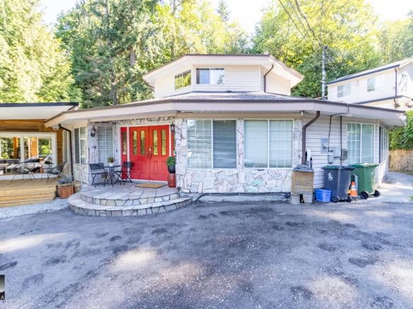 Cozy single-family home exterior with stone accents, vibrant red front door, and spacious porch, situated in a lush, wooded area offering a private setting and curb appeal in Vancouver, BC.