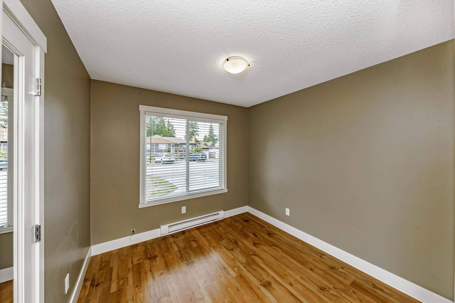 Bright empty bedroom with large window, beige walls, hardwood flooring, and white trim, ideal for Vancouver Island and BC real estate listings.