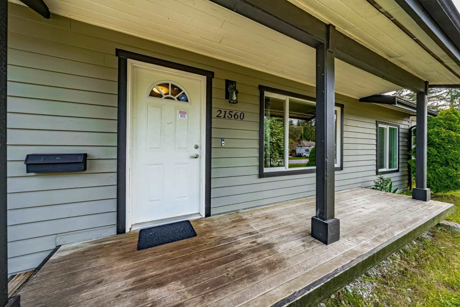 Bright front porch of a modern Vancouver home, featuring a white door, black accents, and a spacious wooden deck, showcasing attractive curb appeal and outdoor living space.