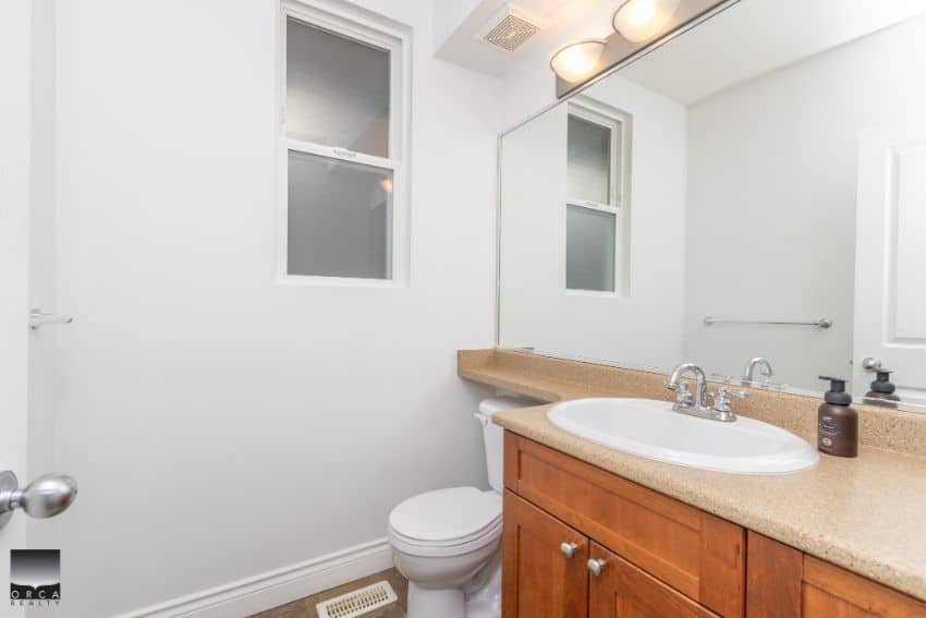 Bright bathroom with white walls, dual small windows, and a wooden vanity with beige countertop in a modern Ottawa home. Perfect for real estate listings.