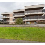 Modern multi-story residential building with balconies and landscaped surroundings in a picturesque urban setting.