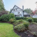 Lush landscaped garden in front of a charming, historic home with vibrant greenery and mature trees, showcasing prime Vancouver Island residential real estate from Orca Realty Inc.