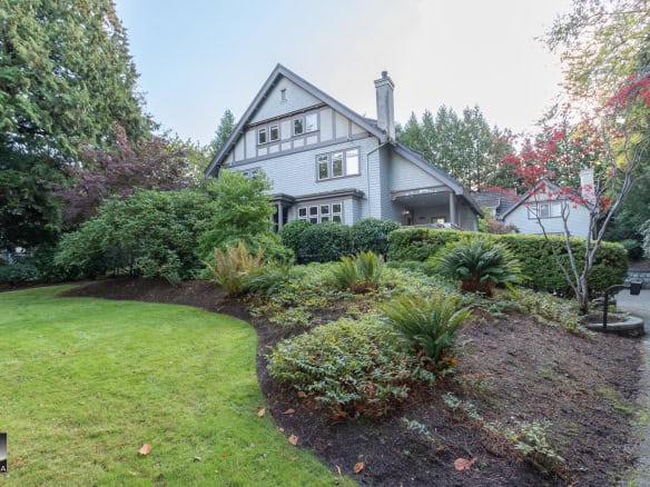 Lush landscaped garden in front of a charming, historic home with vibrant greenery and mature trees, showcasing prime Vancouver Island residential real estate from Orca Realty Inc.