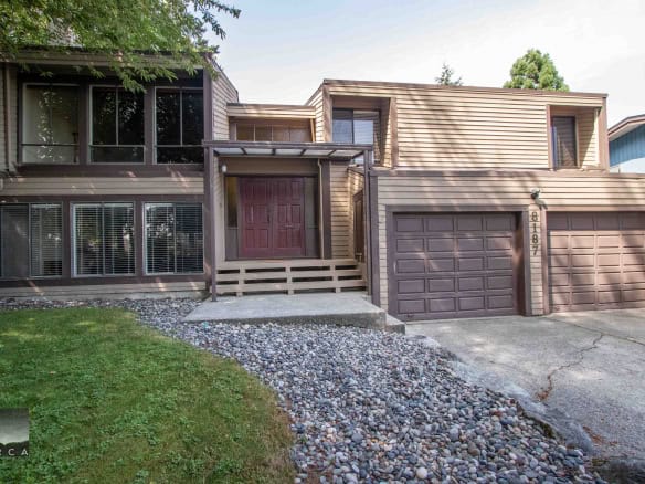 Cozy contemporary multi-level house with a double garage, wooden siding, large windows, and a landscaped front yard in a peaceful neighbourhood - perfect for Vancouver real estate buyers.