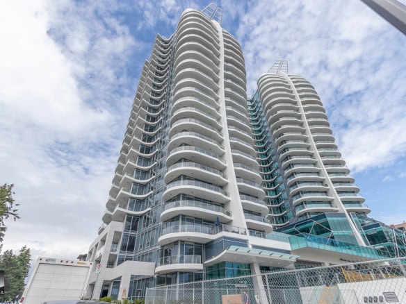 Luxurious modern high-rise condo building with curved balconies, glass exterior, and downtown Vancouver skyline, showcasing premium real estate opportunities in BC.
