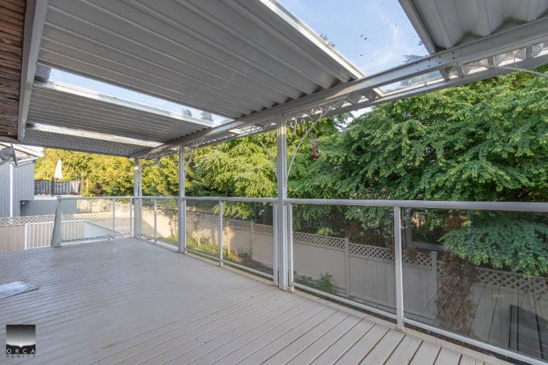 Spacious outdoor balcony with metal roofing and glass railing overlooking lush green trees, perfect for relaxation or entertaining in a Vancouver-area property listed by Orca Realty Inc.