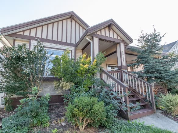 Charming family home with a welcoming porch, surrounded by lush greenery and mature trees, located in a desirable neighbourhood on Orca Realty Inc.'s property listing.