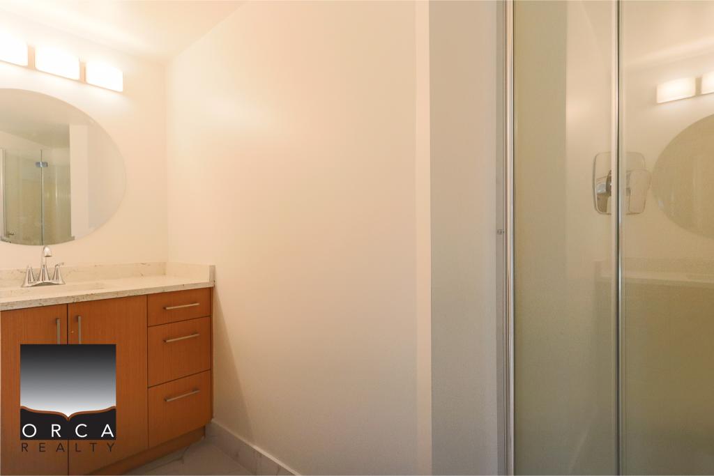 Modern bathroom with wooden vanity, marble countertop, and glass shower enclosure in a contemporary Orca Realty property.