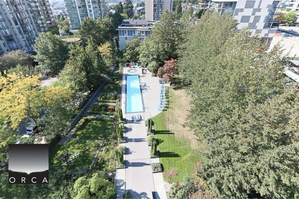 Aerial view of a modern residential complex with a swimming pool, surrounded by lush trees and landscaped gardens, showcasing luxury condo living in Vancouver.