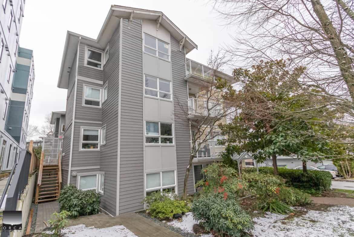 Modern grey multi-family residential building in Vancouver featuring multiple windows and small balconies, surrounded by landscaped greenery and trees, ideal for real estate investment or living.