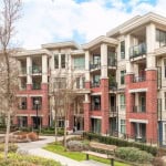 Modern apartment building with brick and beige siding, featuring balconies, large windows, and landscaped outdoor space in Vancouver, BC.