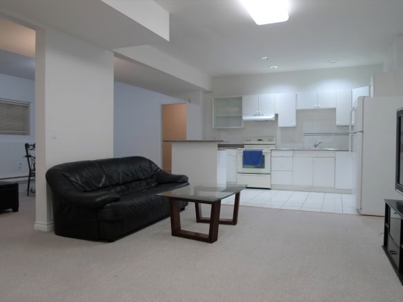 Bright open-concept living space with modern kitchen, ideal for Vancouver real estate buyers and investors. Spacious living room with black leather sofa and large TV, perfect for family gatherings.