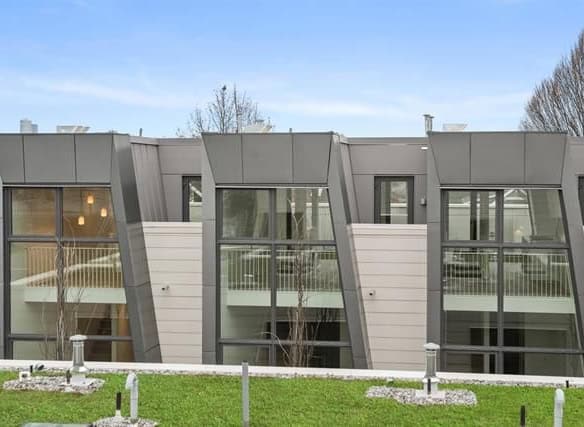 Contemporary modern residential building with large glass windows and unique angular architectural design, located in a scenic suburban area.