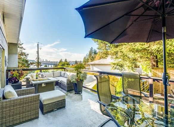 Cozy outdoor balcony with wicker furniture, a large umbrella, and lush greenery, ideal for relaxing and entertaining while enjoying city and natural views.