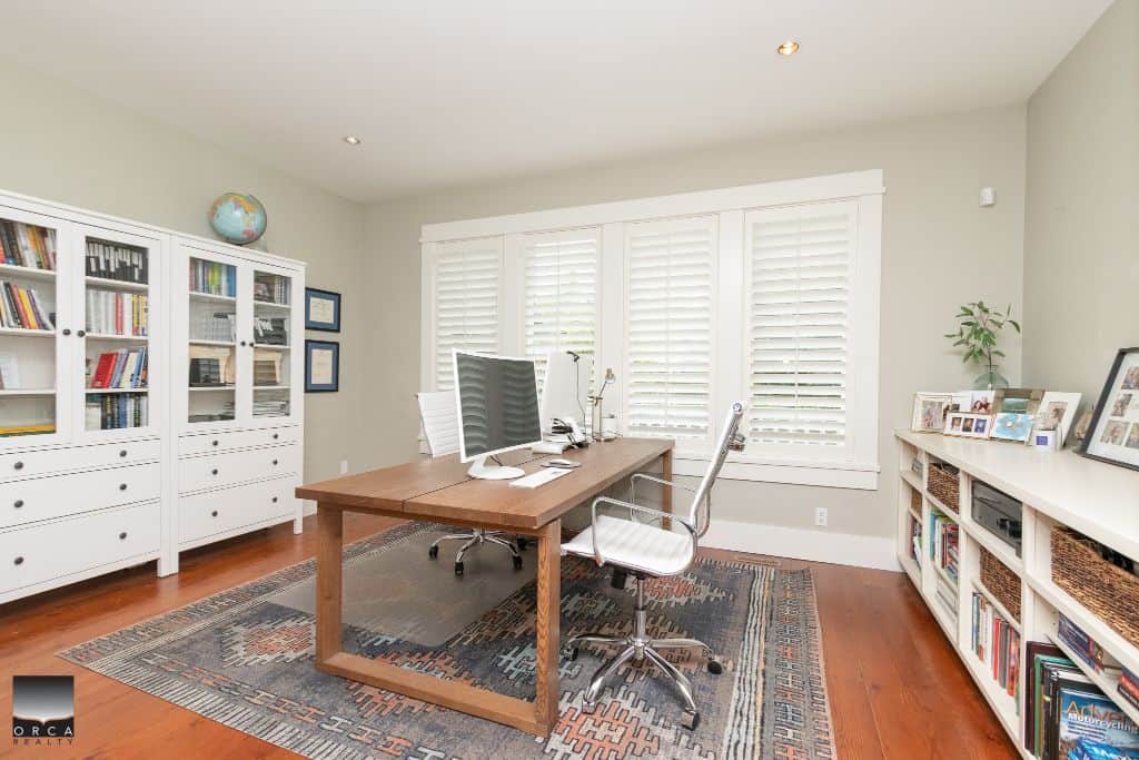 Modern home office interior with wooden desk, white chairs, bookshelves, and large window with white shutters, highlighting professional workspace setup for real estate professionals and homebuyers in Orca Realty Inc.