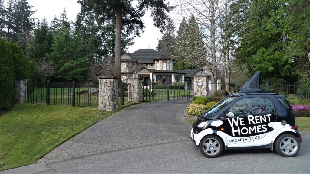 Smart electric car with "We Rent Homes" sign parked in front of a luxury estate, promoting Orca Realty Inc. rental services, Vancouver Island homes, and real estate solutions, with lush landscaped yard.