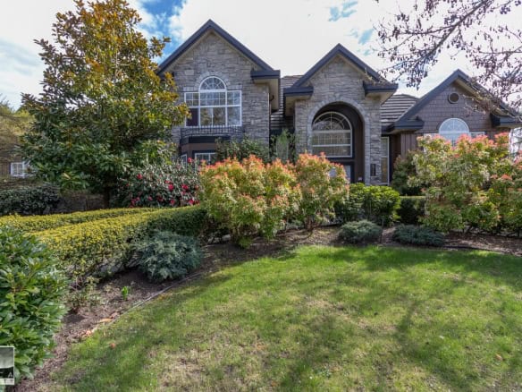 Spacious luxury home with stone facade, manicured garden, vibrant shrubs, and large windows, located in a desirable neighbourhood in Victoria, BC.