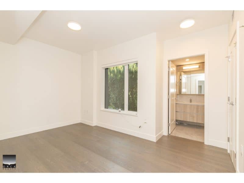 Modern white-painted interior room with large window, natural light, and attached bathroom, showcasing quality Vancouver real estate by Orca Realty Inc. for buyers seeking homes.