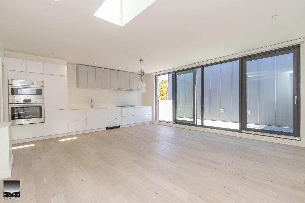 Bright modern kitchen with sleek white cabinetry and large glass sliding doors leading to an outdoor patio, ideal for Vancouver real estate listings.
