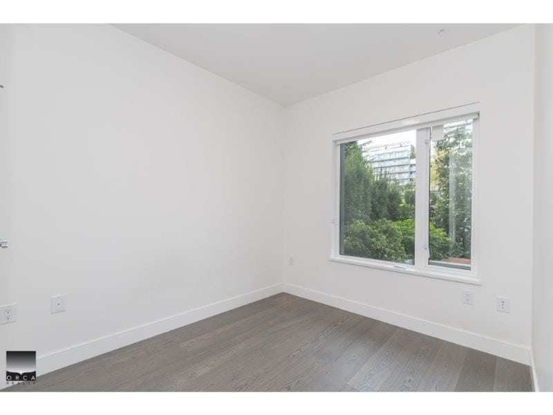 Bright empty bedroom showcasing modern interior design and large window with green city view, ideal for real estate listings by Orca Realty Inc.