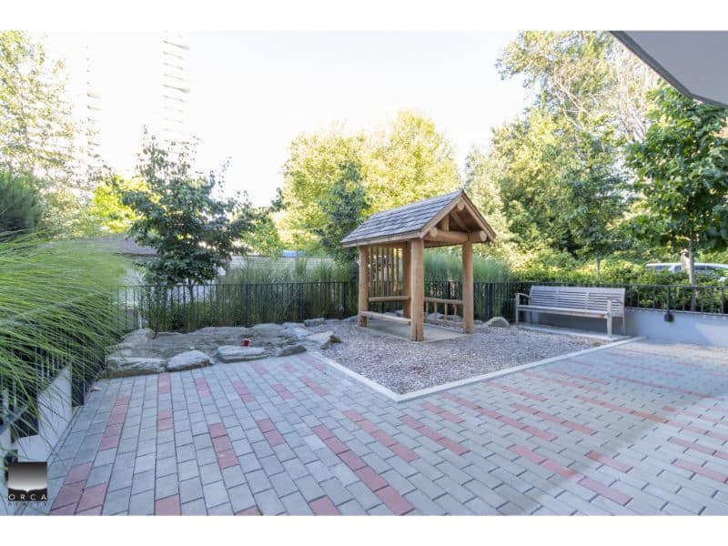 Spacious outdoor patio area with a small wooden playhouse, modern bench, and landscaped greenery, perfect for family recreation and outdoor living in Vancouver's real estate market.