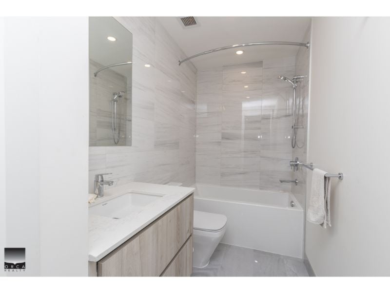 Modern bathroom with white marble tiles, bathtub with shower, sleek vanity and toilet, minimalist design, and contemporary fixtures. Perfect for Toronto real estate listings.