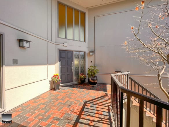 Modern apartment building entrance with a spacious outdoor patio, decorative potted plants, and a black front door, perfect for condo living in Vancouver’s real estate market.