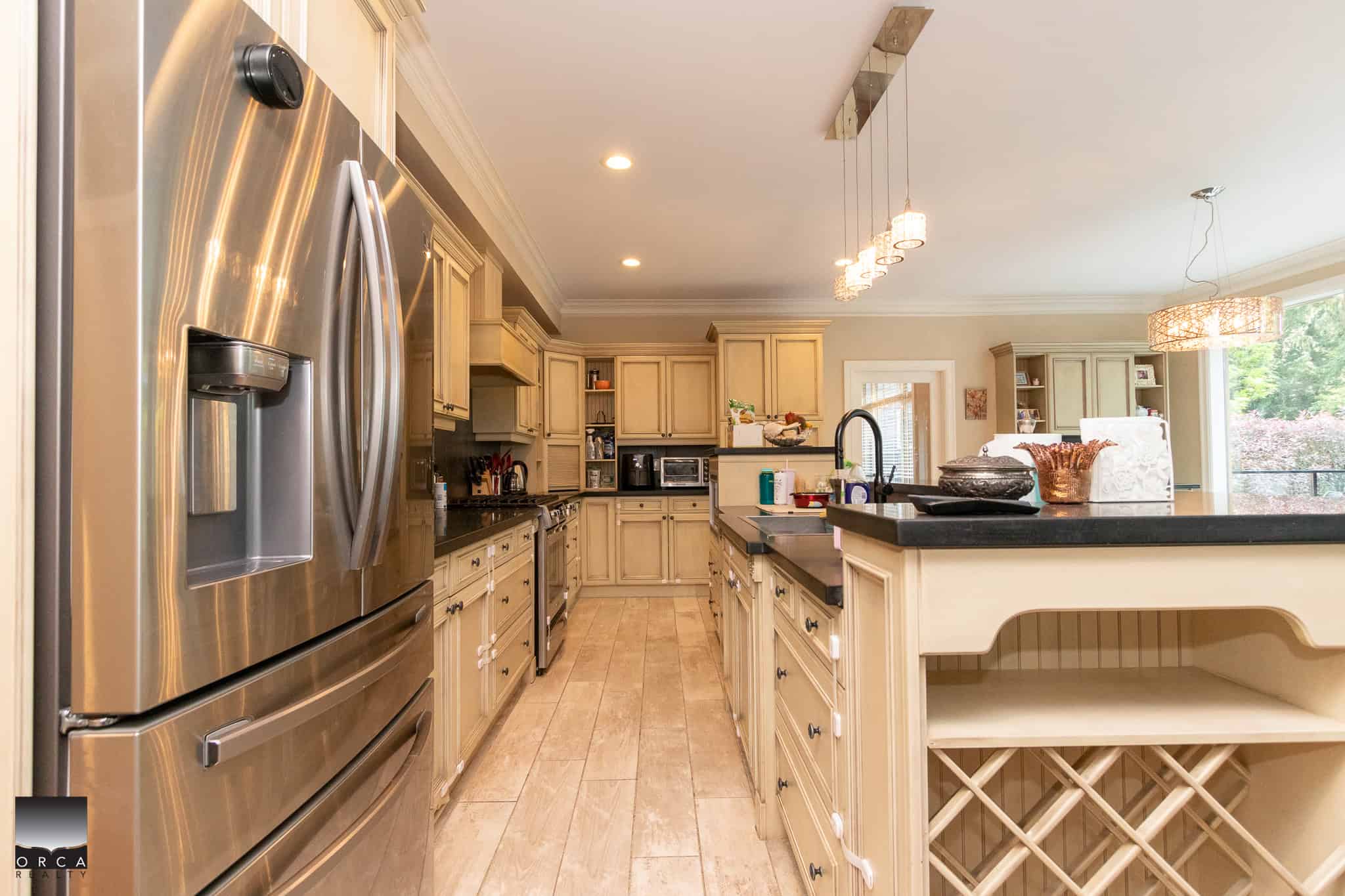 Stainless steel refrigerator in a modern kitchen with cream cabinetry, black countertops, and ample natural light, showcasing upscale home features by Orca Realty Inc.