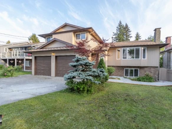 Spacious suburban home with a two-car garage, manicured lawn, and surrounding greenery, perfect for family living and real estate investment in the area.