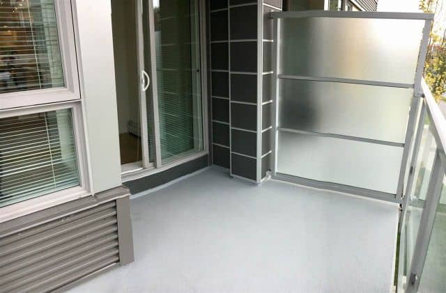 Beautiful small balcony or patio in a modern apartment, featuring glass railing, sliding door, and outdoor storage space, ideal for relaxing or outdoor activities.