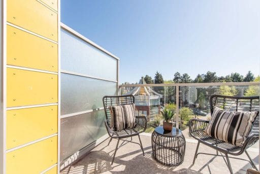 Modern balcony with outdoor seating, black metal chairs, striped cushions, small side table, overlooking lush greenery and elevated view, perfect for relaxation and enjoying outdoor living.