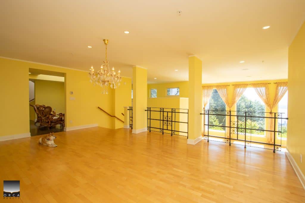 Spacious Bright Living Room with Large Windows and Elegant Chandelier in a Yellow Interior Home for Sale | Orca Realty Inc.