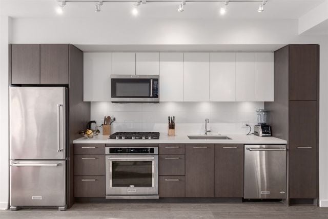 Modern kitchen with stainless steel refrigerator, oven, microwave, and sleek cabinetry in a contemporary condo. Perfect for urban living and home cooking.