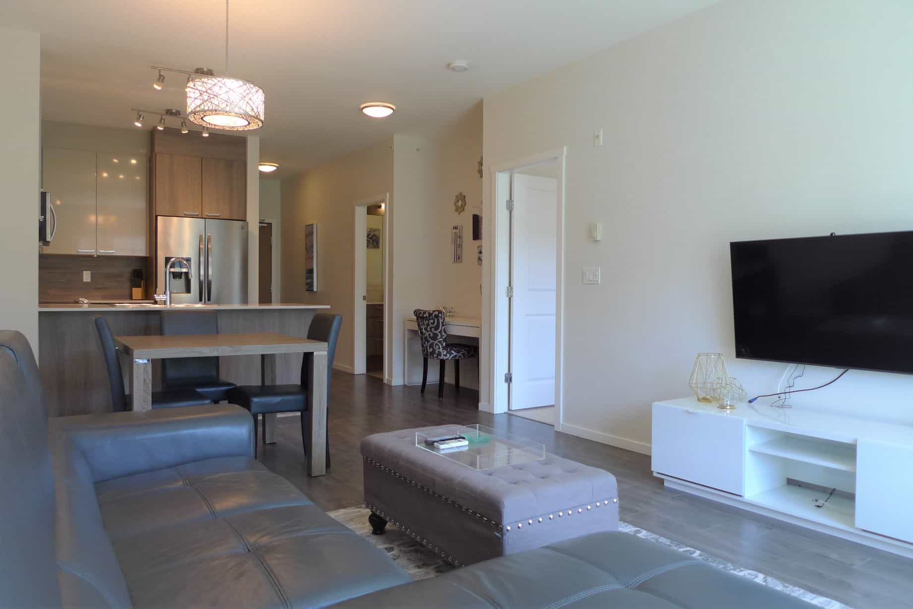 Spacious modern living room with open kitchen, stainless steel appliances, and contemporary decor, showcasing a comfortable home designed for family living and entertaining in Vancouver.