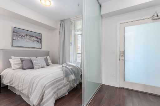 Bright modern bedroom with white bedding, grey accents, and a large window with sheer curtains in a contemporary home.